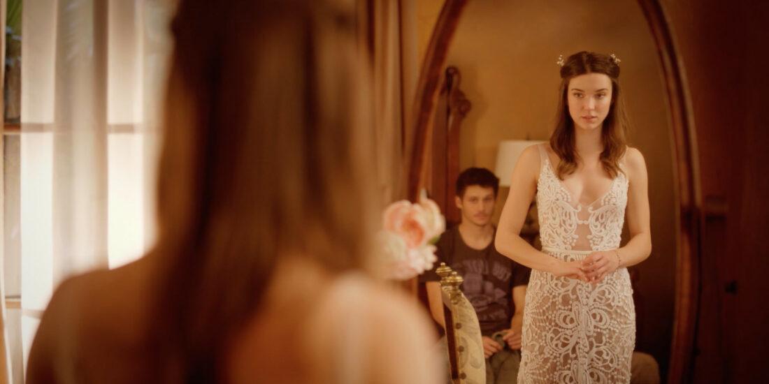 A woman looking into the mirror in a white dress.